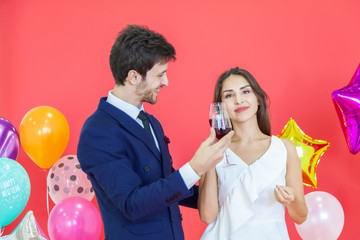 Couple hold in hand wine glass with hapiness face celebrating new party on red background air balloons. Happy New Year and merry x mas valentine woman day concept.