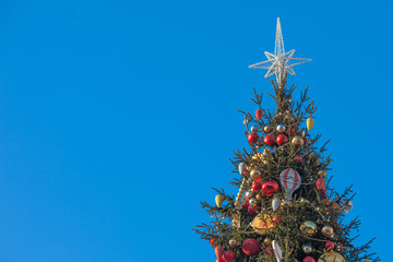 Fototapeta na wymiar Decorated outdoor Christmas Tree with beautiful festive arrangement of fresh spruce with balls. Christmas morning with blue sky. Festive city street decor in winter holidays. Copy space