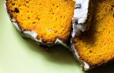 Close up on orange pumpkin pie covered with white icing on green background. Seasonal food.