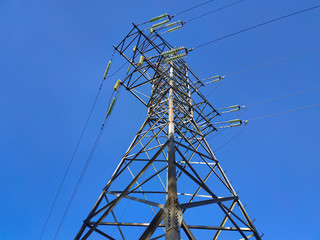 High voltage electricity pylon and transmission power line on the blue sky on the background. Parts of electrical equipment and high voltage power line insulators.