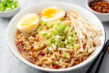 Asian soup ramen with noodles, spring onion, enoki mushrooms and boiled egg in bowl on concrete background. Selective focus.