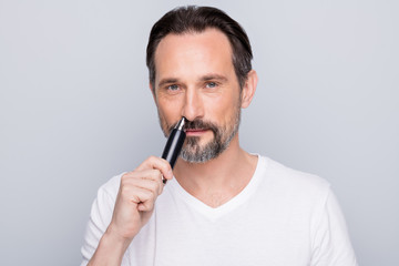 Photo of handsome mature man guy metrosexual hold electric trimmer using to delete nose hair painless procedure wear white t-shirt isolated grey color background