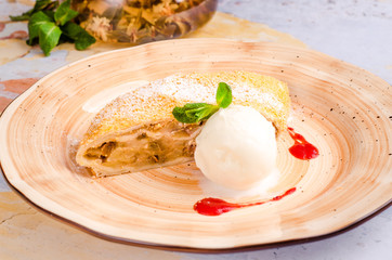Delicious piece of apple strudel with vanilla ice cream, mint and berries on plate, close-up on a background teapot. Fresh baked homemade apple cake