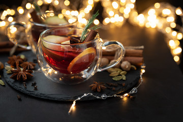 Two cups of Christmas mulled wine or punch with spices and lemon slices on dark wooden background with defocused lights. Christmas or New Year celebration concept