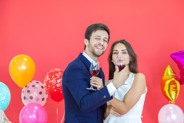 The romantic couple holds in hand wine glass with happiness face celebrating a new year party on a red background and air balloons. Happy New Year and Merry x mas, Valentine, Woman day concept.