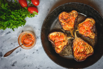 Grilled glazed eggplants on black pan or baking sheet with red sauce, parsley, tomatoes on grey background. Copy text area for menu design. Horizontal top view. Healthy vegetarian snacks concept.