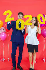 Couple hold in hand year 2020 label with hapiness face celebrating new party on red background air balloons. Happy New Year and merry x mas concept.