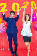 Couple hold in hand year 2020 label with hapiness face celebrating new party on red background air balloons. Happy New Year and merry x mas concept.