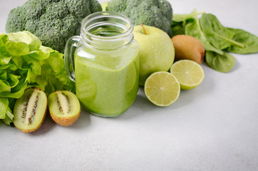 Fresh green smoothie in a jar with ingredients on a gray concrete background.