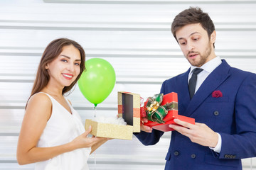 Romantic lovers smiling and exchanging gifts in the midst of a festive celebration that decorated with balloons. Concept of New Year, Christmas, Woman's Day, Valentine Party.
