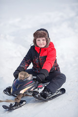 Fototapeta na wymiar Portrait of smiling boy in winter. Warm clothes, fur hat, winter sport. Happy child on a snowmobile.