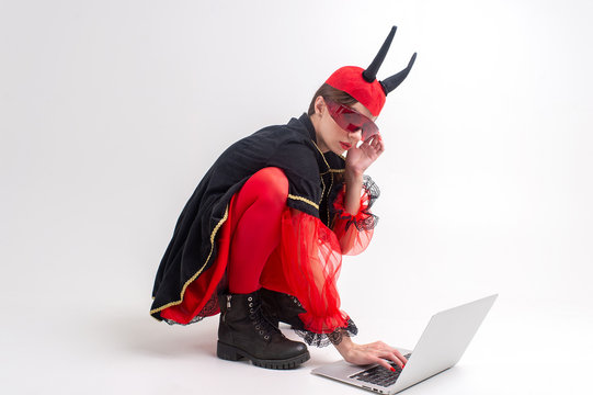 Sexy brunette woman in red tights, black boots and devil horns using laptop over white studio background.