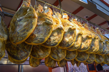 many hams hung from a steel bar at the market counter 