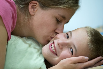 Happy mother gives her son a kiss before sleep and wish good night and beautiful dreams.