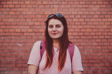 Young girl with red long hair in a summer pink dress on a background of a brick wall in the city