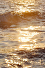 Tropical sunset background. Beautiful colorful ocean wave breaking closing near sand beach. Glare on the water