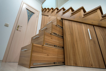 Modern architecture interior with luxury hallway with glossy wooden stairs in multi-storey house. Custom built pullout cabinets on glides in slots under stairs. Use of space for storage.