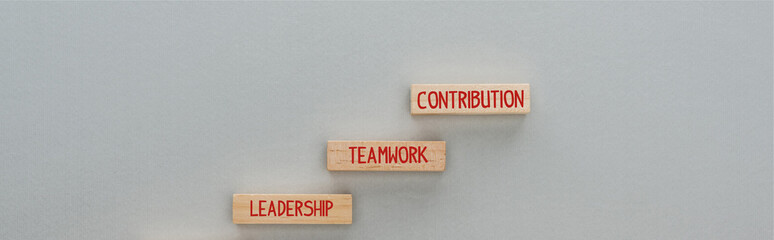 panoramic shot of wooden blocks with leadership, teamwork, contribution words on grey background, business concept