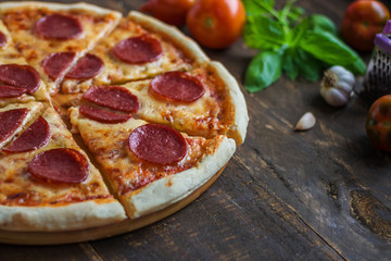 fresh baked sliced pepperoni pizza and ingredient on dark wooden background close up