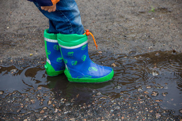 Children's feet in rubber boots in a puddle