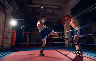 Two aggressive men boxers exercising kickboxing in the ring at the sport club