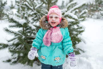 Funny litle girl with her face covered with snow laughing and shouting of cold feelings.