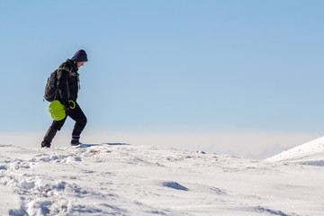 Silhouette of alone tourist walking on snowy mountain top enjoying view and achievement on bright sunny winter day. Adventure, outdoors activities and healthy lifestyle concept.