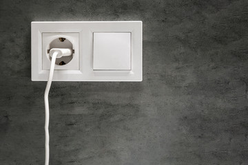 A closeup view of a group of white european electrical outlet with a plug inserted into it and a switch located on a concrete gray wall in a modern bathroom with copy space