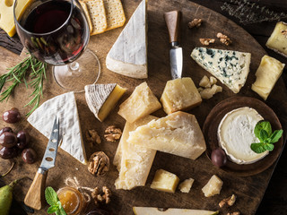 Cheese platter with organic cheeses, fruits, nuts and wine on wooden background. Top view. Tasty cheese starter.