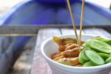 Oval shaped meatball Topping with a spicy cucumber and skewers in a white foam cup placed on the wood.