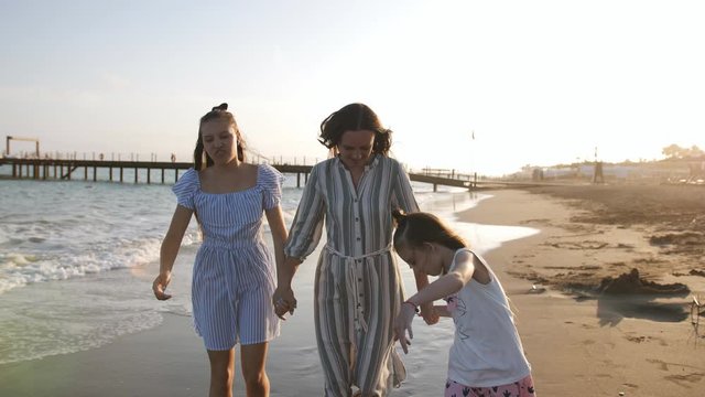 Happy Mother with two daughters 7 and 13 years of walking on the sandy shore at sunset.