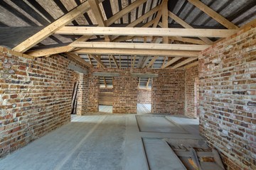 Attic of a building under construction with wooden beams of a roof structure and brick walls.