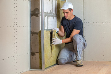 Worker insulating a room wall with mineral rock wool thermal insulation.