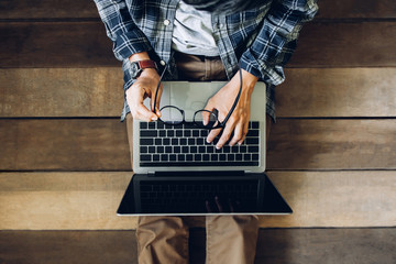 businessman sitting on wooden floor holding glasses using laptop working at home to send and send...