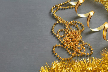 Golden tinsel, ribbon and glossy long beads lies on dark scratched concrete desk. Space for text. Top view