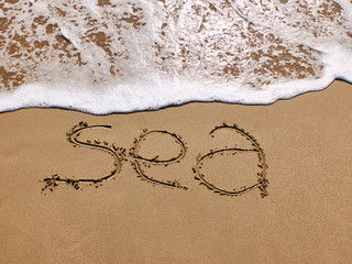 Inscription Sea on the sandy beach and foamy sea water