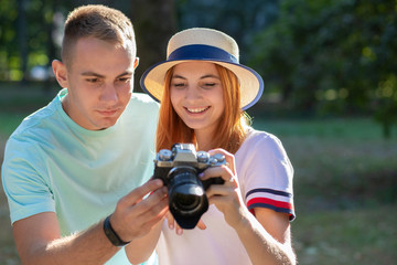 Young teenage couple taking pictures of one another outdoors in sunny summer park.