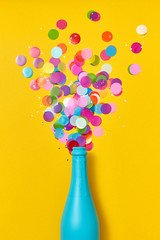 Multicolored confetti as a bubble foam above open champagne bottle.