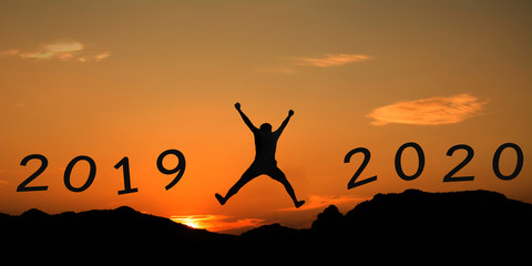 sunset with mountain silhouette and man jump on new year 2019 cross to 2020
