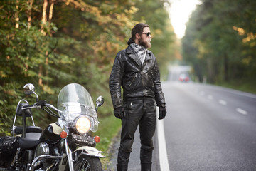 Profile bearded athletic long-haired motorcyclist in black leather outfit and dark sunglasses...