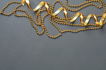 Golden ribbon and glossy long beads lies on dark scratched concrete desk. Space for text. Top view
