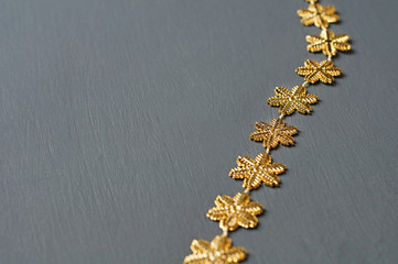 Row of golden glossy beads in form of snowflakes lies on dark scratched concrete desk. Space for text