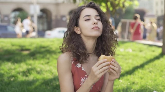 Beautiful brunette with curly hair eats a delicious burger