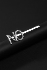 Subject shot of a silver hair clip made as a sign plate with sparkling crystal lettering "NO" on the black silky tube on the black background. 