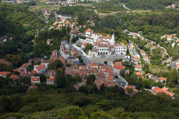 Fototapeta na wymiar View from the fortress wall of the castle of the Moors. View of the small town of Sintra near Lisbon. Top view of a cozy village with red roofs in the middle of a green valley and forest.
