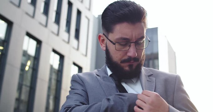 Caucasian businessman in glasses, suit and tie taking out his smartphone from an inner pocket and being happy as got good news in the message or e-mail. Close up.
