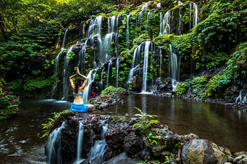 Woman sitting on the rock, practicing yoga. Young woman raising arms with namaste mudra near...