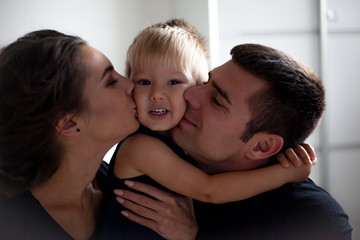 The caucasian family hugging in the home bedroom and kissing the baby. People dressed black clothes, pajamas