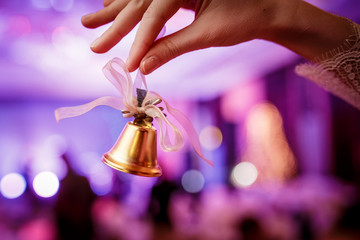 Close-up girl holds in hand a golden Christmas bell on lights background