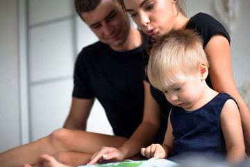 Happy family sit in the bed on home bedroom and reading the book to baby.